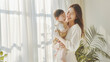 Young asian mother holding her child and smiling. Light minimal styled interior, place for text.