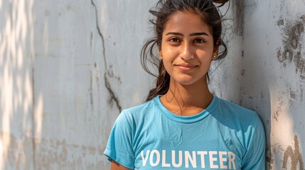 Wall Mural - Young woman with dark hair smiling against a textured wall wearing a light blue t-shirt with the word 