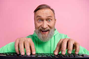 Photo portrait of cool pensioner man excited typing keyboard dressed stylish green clothes isolated on pink color background