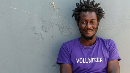 Wall Mural - Man with dreadlocks wearing a purple volunteer t-shirt smiling against a textured gray wall.