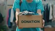 © iuricazac - Person holding a box of donations possibly in a thrift store or donation center with a focus on the act of giving and the importance of second-hand clothing and items.