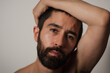© Levi Meir Clancy - A man looks nervously at the camera with his brow slightly furrowed. He has his arm raised, with his hand wrapped around his tilted head. Being shirtless, he looks concerned and vulnerable.