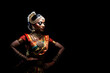 An Indian classical dancer in traditional attire striking a dynamic pose against a black background.