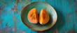 Two pieces of exotic tropical fruit, mamey and zapote, are showcased on a plate, offering a refreshing and delightful combination. The mamey is delectable and the zapote juicy, providing a taste of