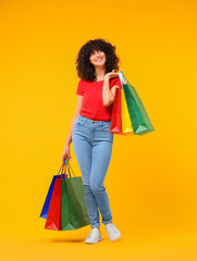 Wall Mural - Happy young woman with shopping bags on yellow background. Space for text