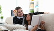 Portrait of attractive happy friends discussing something interesting and reading book. Cozy atmosphere at home. Girls having fun together gossiping sitting on sofa