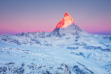 First sunrays on the snowy peak of Matterhorn mountain  with pink sky at sunrise in the Swiss Alps