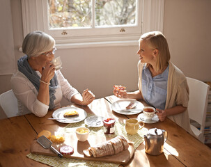 Poster - Happy woman, senior mother and eating breakfast, drinking coffee and conversation at home together. Smile, elderly mom and daughter with tea cup at table, food and family with healthy cheese on bread