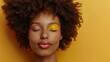 Beautiful black fashion model portrait featuring a brunette young woman with an afro hair style, closed eyes, and creative yellow make-up.