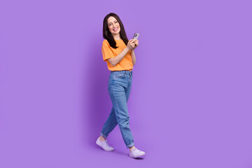 Wall Mural - Full length body photo of strolling cheerful business woman busy browsing smartphone news feed isolated on violet color background