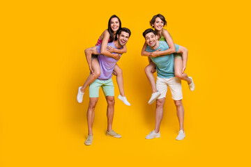 Wall Mural - Full body photo of positive cheerful guys piggyback girlfriends isolated over vibrant color background