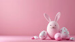 Tarjeta de huevos de pascua pintados de colores, junto a huevo decorado como un conejo con grandes orejas, sobre superficie y fondo rosa