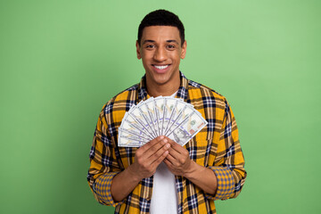 Sticker - Portrait of young cheerful business man wearing checkered yellow shirt holding first million dollars isolated on green color background