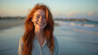 Portrait of beautiful girl with long red hair, smiling and looking at camera against seascape sunset.