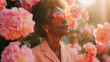Portrait of a black senior woman in sunglasses, wearing a peach suit, surrounding big pink flowers.