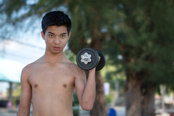 Asian plump young man lifts four-kilogram and eight-kilogram dumbbells to exercise and loose weight in an open courtyard in late afternoon, health care and recreational activity concept.