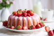 Round pound cake baked in bundt cake mold with pink glazing and strawberries on table