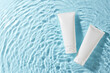 © Goncharuk film - Natural beauty: embracing organic cosmetics. Top view shot of two white skincare tubes floating on a serene blue water background, offering ample space for promotional content