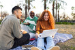 © ADDICTIVE STOCK - Diverse students enjoying picnic with laptop in park