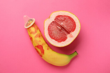 Wall Mural - Half of grapefruit, banana with condom and red lipstick marks on pink background, flat lay. Safe sex concept