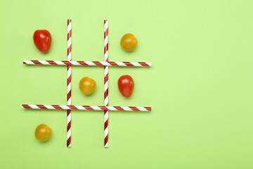 Wall Mural - Tic tac toe game made with cherry tomatoes on light green background, top view