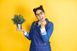 Young caucasian gardener woman holding a plant isolated on yellow background showing middle finger doing fuck you bad expression, provocation and rude attitude. screaming excited