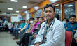 Indian doctor seated outside busy clinic, patients waiting in line