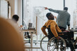 © qunica.com - A diverse workplace with a person using a wheelchair interacting with a colleague by the window. Focus on accessibility and teamwork.