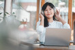 © Satori Studio - Business freelance concept,A contented woman with headphones enjoys music as she works on her laptop at a well-lit table with a coffee and plant nearby.