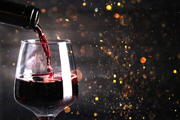 Sticker - Pouring red wine into glass against dark background with blurred lights, closeup. Space for text