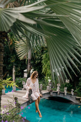 Wall Mural - Woman have a rest and chill in the pool with amazing view on the jungle sit on the wooden bridge and look on blue water of swimming pool