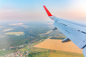 View of airplane wing, blue skies and green land during landing. Airplane window view.