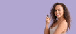 Beautiful African-American woman holding hair spray on lilac background with space for text