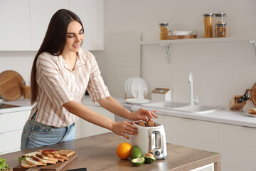 Wall Mural - Young beautiful happy woman making tasty toasts in kitchen