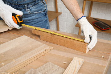 Wall Mural - Female carpenter measuring plank length with tape in workshop, closeup