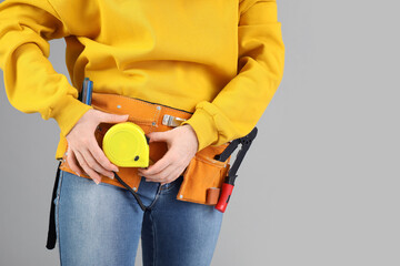 Wall Mural - Female construction worker with measuring tape and tools on grey background, closeup