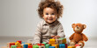 Joyful curly-haired toddler with colorful blocks and plush bear, child's play and learning.