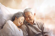 An elderly Asian man and woman are laying together on a bed, showcasing love and companionship in their golden years