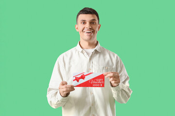 Poster - Young man with gift voucher on green background