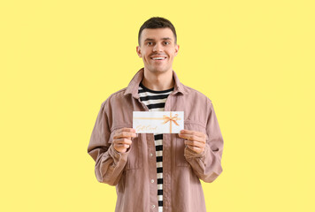 Canvas Print - Young man with gift card on yellow background