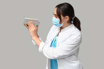 Canvas Print - Young female dentist in mask with dental shade guide on grey background