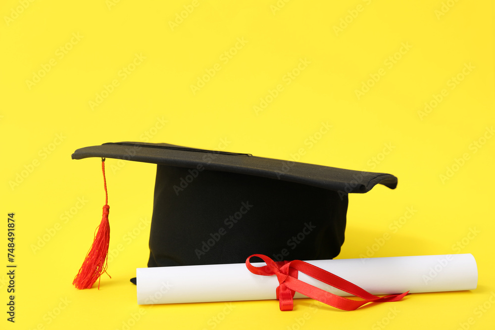 Mortar board and diploma on yellow background
