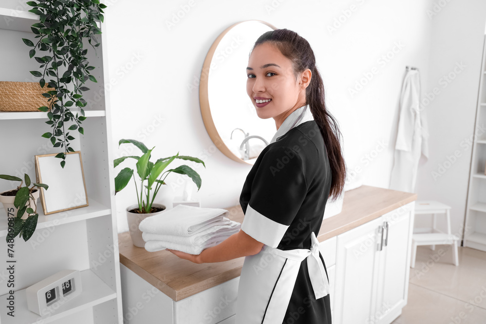 Young Asian chambermaid putting clean towels on table in bathroom