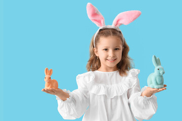 Wall Mural - Cute little girl in bunny ears with toys rabbit on blue background. Easter celebration