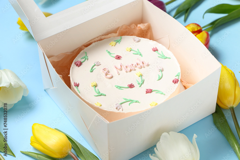 Box with sweet bento cake and beautiful tulips on blue background. International Women's Day