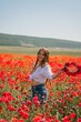 © svetograph - Happy woman in a poppy field in a white shirt and denim skirt with a wreath of poppies on her head posing and enjoying the poppy field.
