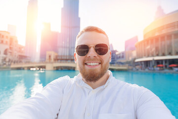 Wall Mural - UAE business tourism for cryptocurrency concept. Happy young crypto businessman man tourist in sunglasses background skyscrapers in Dubai
