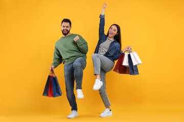 Wall Mural - Excited couple with shopping bags having fun on orange background