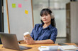 © Wasana - A focused professional woman listens to music with headphones, holding a coffee cup while taking a break at her workspace.