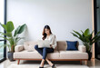 © anmitsu - Beautiful young Asian female freelancer successful in business sitting on comfortable sofa and browsing internet through laptop. She has luxury interior, work from home concept